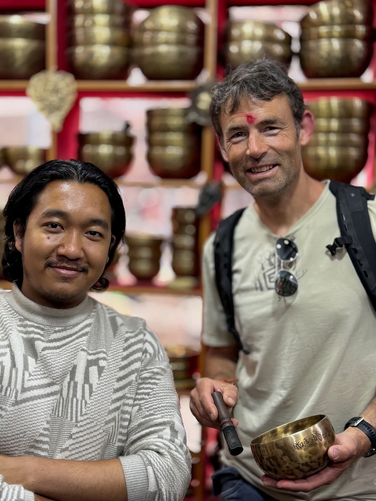 Simon Jackson in a Kathmandu singing-bowl shop, holding a brass bowl and striker beside the shopkeeper